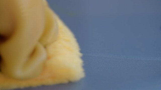 Closeup hand wiping blue scale platform with soapy yellow sponge removing dirt and residue, slow deliberate strokes, household cleaning routine, focused texture of foam and wet