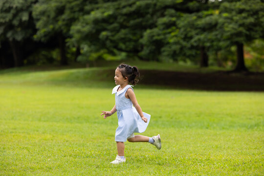 child runs in summer field, small child running and playing on the lawn. spending time with father in the park. Happy Asian family having fun time on picnic at city nature park, outdoor activitie