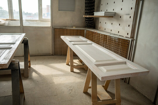 Painting area in restoration workshop, reconstructed antique wooden doors drying out after painting, professional drying zone in woodworking studio, vintage doors lying on construction sawhorses.