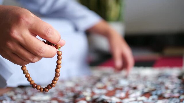 Close-up of hands reciting dhikr using prayer beads against a blurred background. Hands reciting dhikr. A man reciting dhikr while holding a prayer beads. A Muslim's worship activity.
