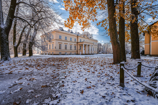 The New Castle in Kostelec nad Orlici surrounded by autumn park with first snow. Beautiful empire style chateau architecture with golden leaves and snowy ground under a blue sky.