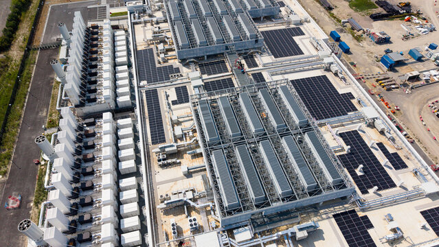 Aerial view of a large hyperscale data center facility featuring rows of cooling units, solar panels on the roof, and industrial infrastructure in Settala, Lombardy, Italy.