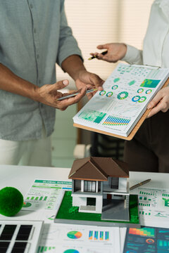 Real estate developer and investor planning sustainable housing project with ESG dashboard and green house model.