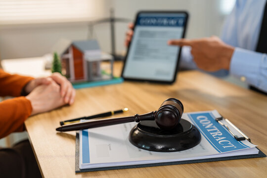 Real estate agent or lawyer explaining property contract conditions to client before signing with house model on desk.