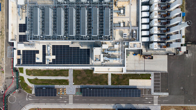 Aerial view of a modern hyperscale data center featuring extensive rooftop cooling infrastructure and solar panel arrays, situated in an industrial area in Settala, Lombardy, Italy.
