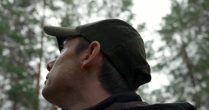Male traveler searching the way and looking up at pine trees