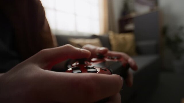 Hands of teenager playing video game, pressing buttons on red controller in living room. Footage ideal for gaming industry commercials, console marketing, and youth lifestyle videos