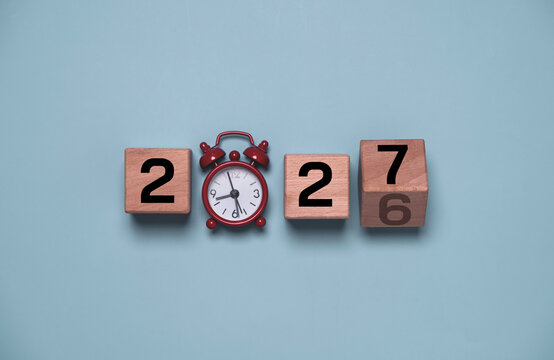 New year 2027 concept with wooden calendar blocks and vintage alarm clock on a blue background, symbolizing time management, planning, goals, countdown, business strategy, productivity and beginnings.