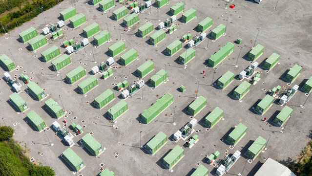 Aerial view of a large battery energy storage system facility with rows of green containers on a gravel site in Tavazzano con Villavesco, Lombardy, Italy.