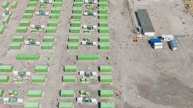 Aerial view of a Battery Energy Storage System BESS facility with rows of green storage containers and electrical infrastructure on a gravel site in Tavazzano con Villavesco, Lombardy, Italy.