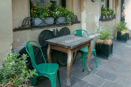 Weathered wooden table and green metal chairs create a cozy street cafe setting in Krakow, Poland. Window boxes contain variegated wintercreeper, ivy and flowering calibrachoa, while aged plaster wall