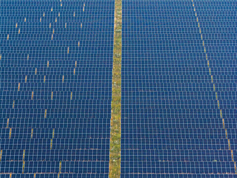 Aerial view of a solar farm producing green energy with rows of photovoltaic panels and a narrow grassy path in Poland.