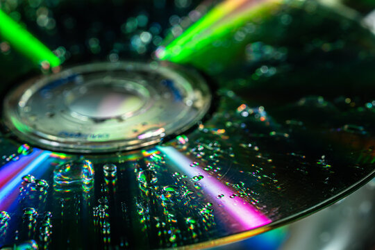 Close up of a compact disc covered with water droplets and colorful rainbow light reflections. Concept data storage, optics, technology, texture, science, background, and digital media.