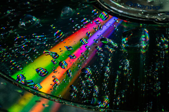 Close up of a compact disc covered with water droplets and colorful rainbow light reflections. Concept data storage, optics, technology, texture, science, background, and digital media.