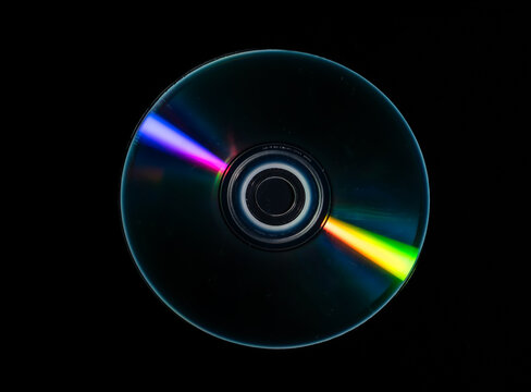 Top view of a compact disc displaying vivid rainbow light reflections across its reflective surface. Concept data storage, digital media, optical technology, nostalgia, background and spectrum.