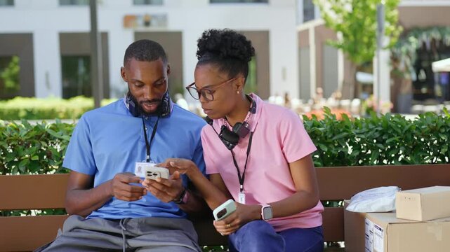 Two couriers reviewing delivery updates on a smartphone during a short work break. Teamwork, parcel delivery, and efficient last-mile logistics concept.