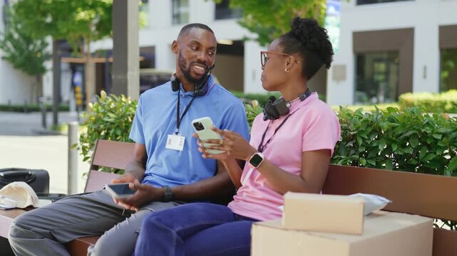 Two couriers comparing delivery orders on a smartphone while taking a break outdoors. Parcel delivery, teamwork, and daily logistics coordination.