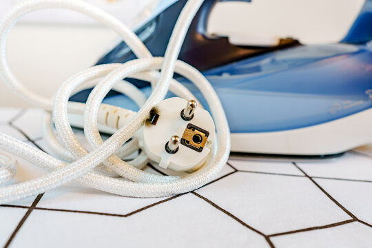 A close up shot of a burnt electrical plug with scorch marks resting with its braided cord in front of a blue steam iron.