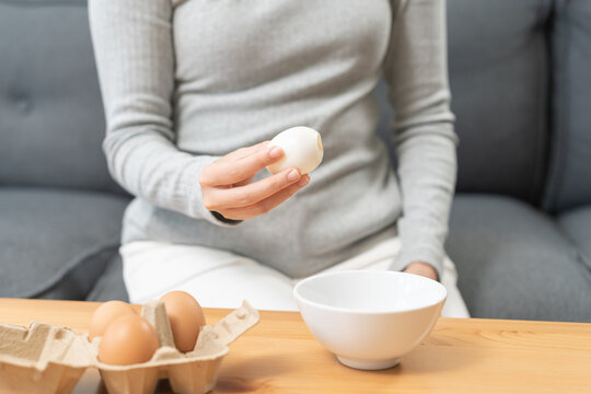 Protein in food, keto diet asian young woman hand peeling, shelling chicken boiled egg, prepares ingredient for breakfast meal on table at home. Removing egg shell, cleaning egg, health care concept.