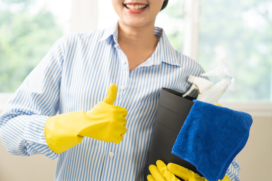 Cleaning professional housekeeping concept. Asian young woman wearing yellow gloves, hand show thumb up with tool bucket, smile girl looking at camera after doing housework or chores at home, job done