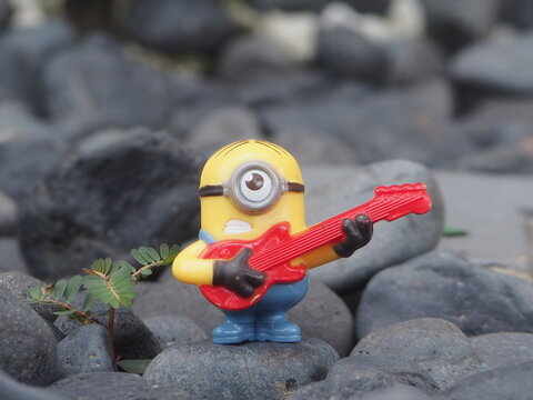 Indonesia - May 18, 2025 : Mini toy of action figure at outdoor with blurred background. Miniature photography concept design. Minifigure of Minion character playing guitar at nature. Relaxing concept