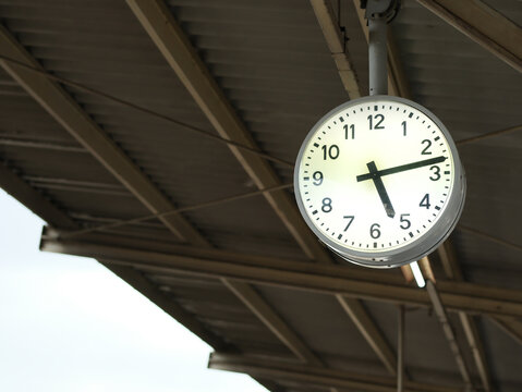 Station Clock, Timepiece Above: A circular white clock with black numbers and hands hangs from the corrugated metal roof of a train station, indicating 4:20.