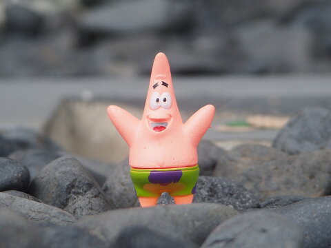 Indonesia - May 18, 2025 : Mini toy of action figure at outdoor with blurred background. Miniature photography concept design. Minifigure of Patrick Star character from Spongebob Squarepants film.