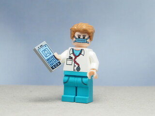 Naklejka premium Indonesia - May 16, 2025 : Mini toy of action figure at table with blurred background. Miniature photography concept design. Minifigure of professional doctor character hold the smartphone at hospital