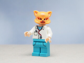 Naklejka premium Indonesia - May 16, 2025 : Mini toy of action figure at table with blurred background. Miniature photography concept design. Minifigure of orange cat character wearing doctor costume. Healthcare crew.
