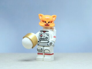 Naklejka premium Indonesia - May 16, 2025 : Mini toy of action figure at table with blurred background. Miniature photography concept design. Minifigure of Orange Cat character wearing astronaut suit at outer space.