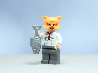 Fototapeta premium Indonesia - May 16, 2025 : Mini toy of action figure at table with blurred background. Miniature photography concept design. Minifigure of orange cat character wearing chef costume with pan and fish.