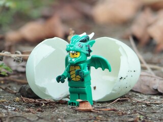 Fototapeta premium Indonesia - May 3, 2025 : Mini toy of action figure at outdoor with blurred background. Wild photography concept design. Minifigure of Baby Green Dragon character coming out from egg. New born concept