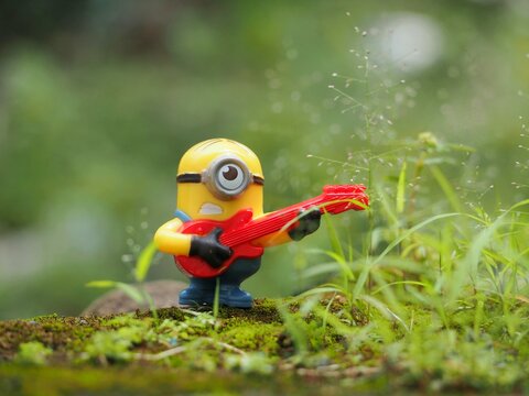 Indonesia - February 14, 2023 : Mini toy of action figure at grassland with blurred background. Toy photography concept. Minions character with guitar at outdoor conceptual design. Playing music.