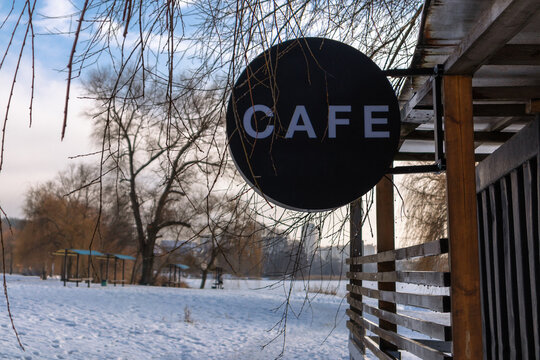 Black round cafe sign on wooden terrace in winter landscape