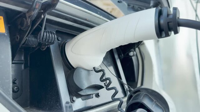 An electric vehicle charging plug is securely connected to the car port. This simple act of recharging represents a hopeful, cleaner, and sustainable future for our planet.