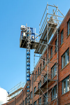 Multi-story brick building with facade scaffolding and construction hoist during building work