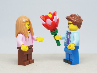 Fototapeta premium Indonesia - March 4, 2026 : Mini toy of action figure at outdoor with blur background. Miniature photography concept design. Minifigure of man character give bouquet of flower to young girl.
