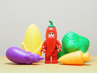 Fototapeta premium Indonesia - February 10, 2026 : Mini toy of action figure at outdoor with blur background. Miniature photography concept design. Minifigure of red chilli guy character with various vegetable.