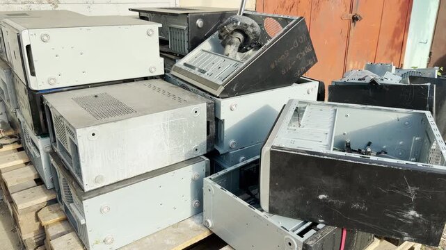 Old computer cases are piled on wooden pallets. These discarded machines feel forgotten and dusty, representing a sense of industrial obsolescence and past technology waiting for recycling.