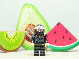 Obraz premium Indonesia - December 5, 2025 : Mini toy of action figure at outdoor with blurred background. Miniature photography concept design. Minifigure of Ninja Go character with Avocado, Water Melon and Kiwi.