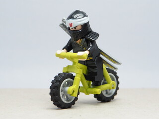 Fototapeta premium Indonesia - December 1, 2025 : Mini toy of action figure at outdoor with blurred background. Miniature photography concept design. Minifigure of Ninja Go character riding the mountain bike at outdoor