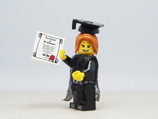 Fototapeta premium Indonesia - November 24, 2025 : Mini toy of action figure at table with blurred background. Miniature photography concept design. Minifigure ofwoman student with graduation gown, cap and certificate.
