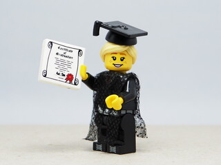 Fototapeta premium Indonesia - November 24, 2025 : Mini toy of action figure at table with blurred background. Miniature photography concept design. Minifigure of woman student with graduation gown, cap and certificate.