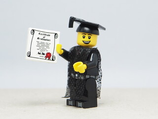 Obraz premium Indonesia - November 24, 2025 : Mini toy of action figure at table with blurred background. Miniature photography concept design. Minifigure of student with graduation gown, cap and certificate.