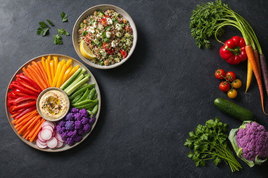 Vegetable rainbow platter and quinoa salad bowl on dark slate, healthy plant-based eating