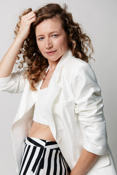 An authentic middle aged woman with natural skin poses confidently in a white blazer. Concept for real beauty, aging gracefully, self acceptance, and diversity in modern lifestyle.