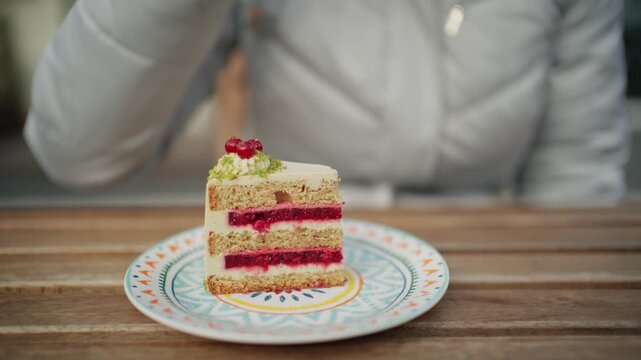 Woman eating slice of layered berry cream cake on wooden table at cafe terrace during winter season.
