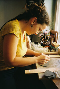 A woman bends over her craft, shaping a piece of clay