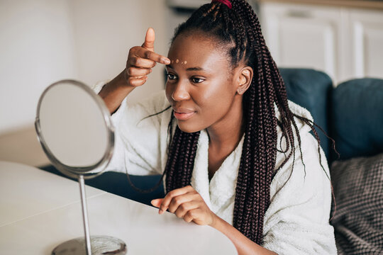 Happy smiling african american woman applying foundation at home