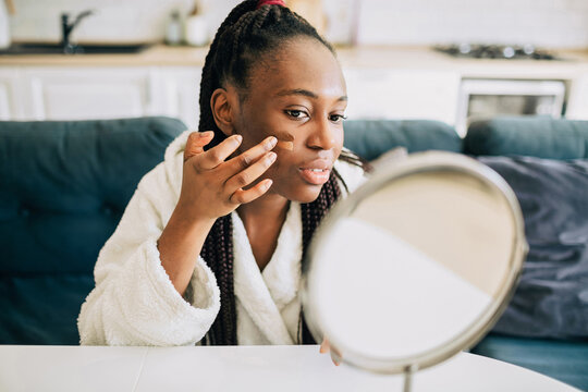 Portrait of happy african american woman putting on foundation at home